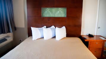 Habitación de hotel con una cama grande, un cabecero de madera, un escritorio pequeño con teléfono y aire acondicionado de pared.