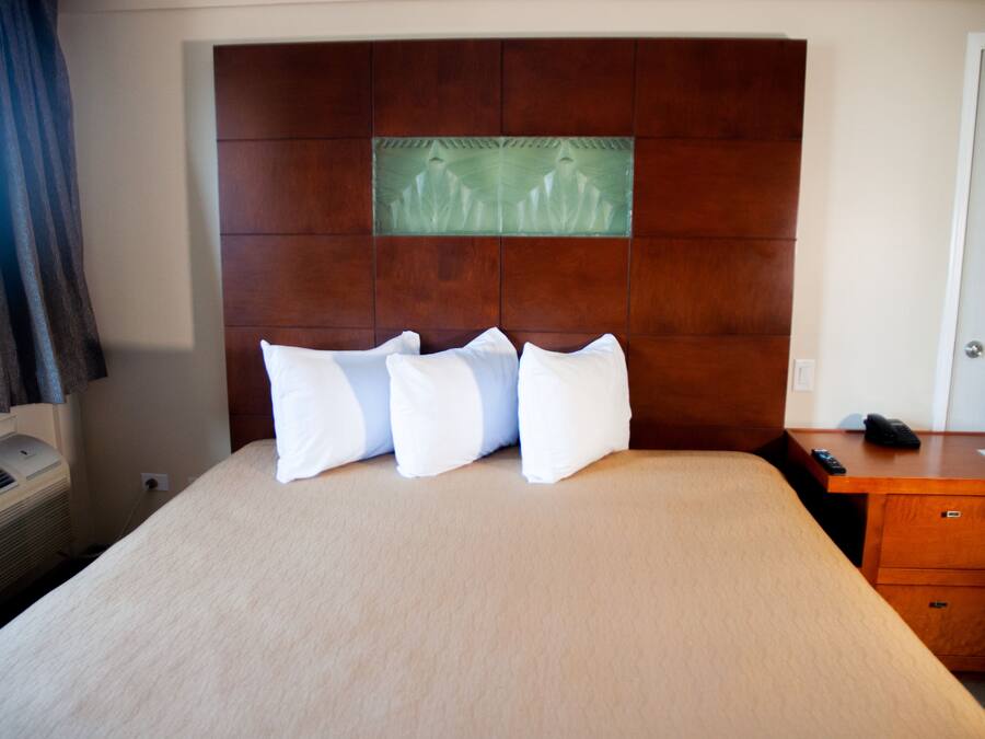 Habitación de hotel con una cama grande, un cabecero de madera, un escritorio pequeño con teléfono y aire acondicionado de pared.