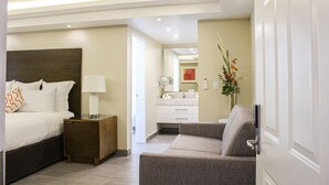 Une chambre d’hôtel moderne équipée d’un lit, d’une table de chevet, d’une petite table et d’un coin salon avec un fauteuil.