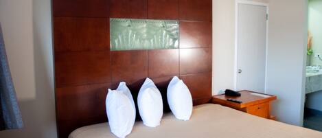 A hotel room with a wooden headboard, a bed with white pillows, a wooden nightstand with a phone, and a door leading to a bathroom.