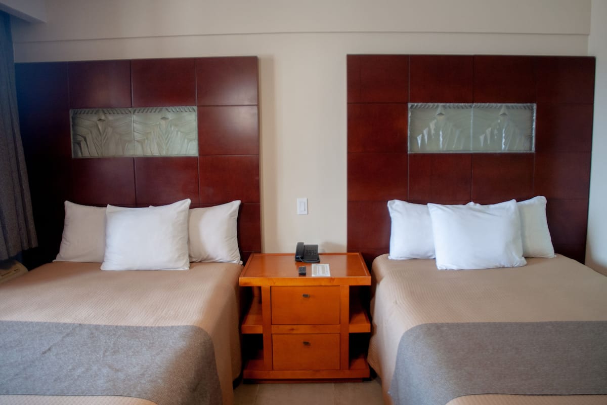 A hotel room with two beds, a wooden nightstand, and a telephone.