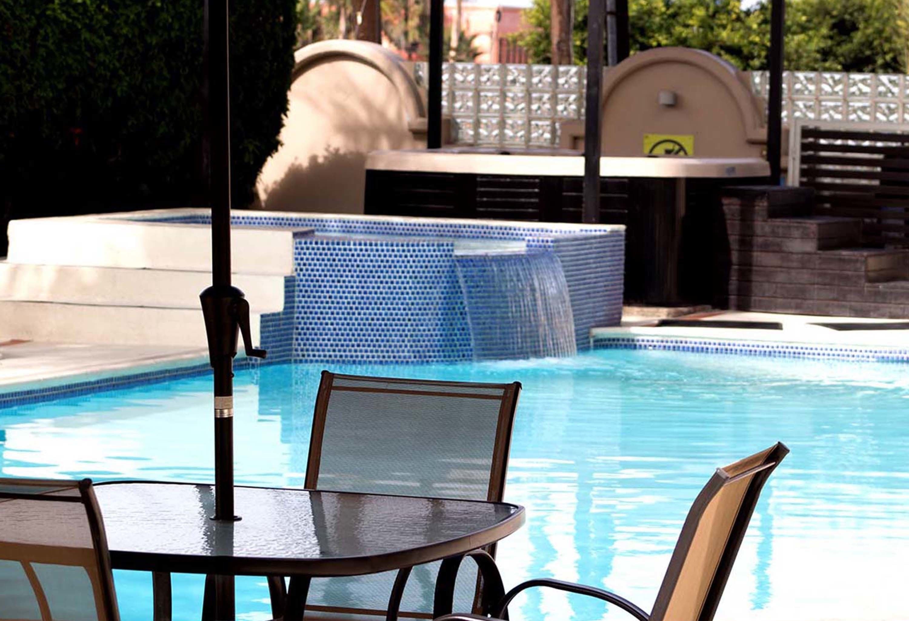 Zona de piscina con mesa y sillas, fuente de agua y área de descanso cubierta.