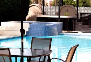 A pool area with a table and chairs, a water feature, and a covered seating area.