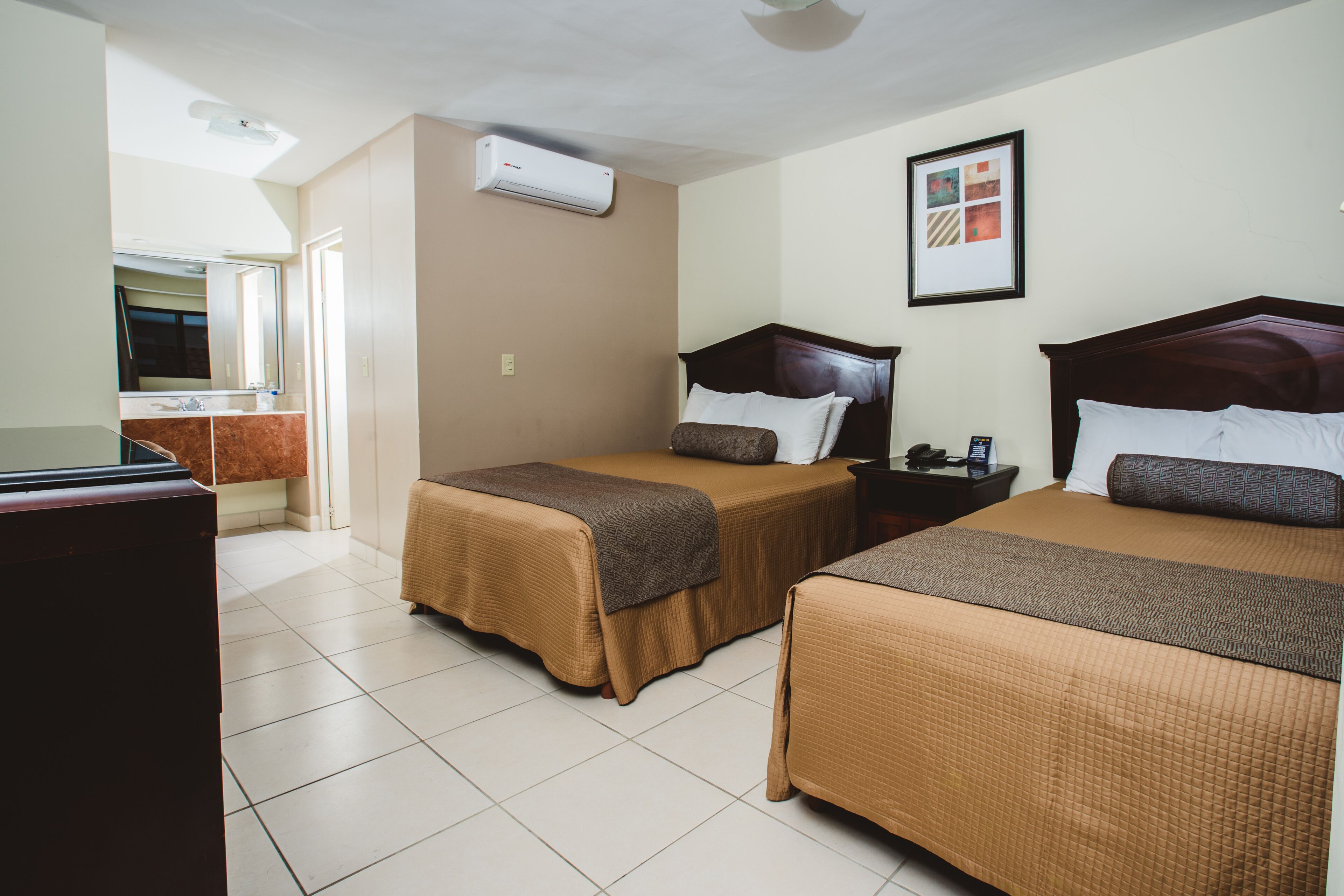 A hotel room with two beds, a TV, and an air conditioning unit.