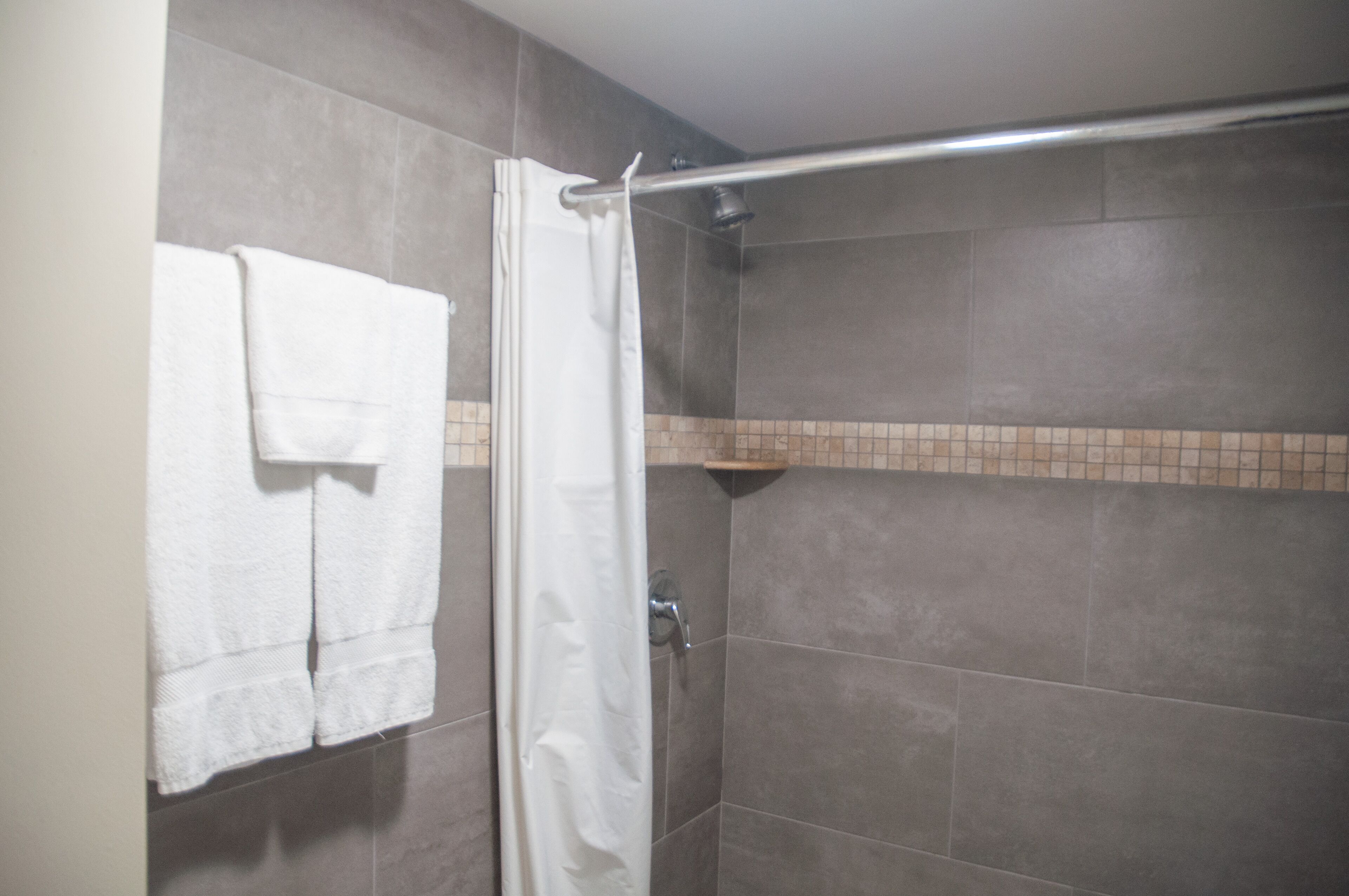 A shower area with a white shower curtain, a towel rack with two towels, and a showerhead.