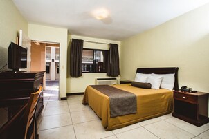 Habitación de hotel con cama, escritorio, silla, televisión, mesita de noche y ventana con cortinas.