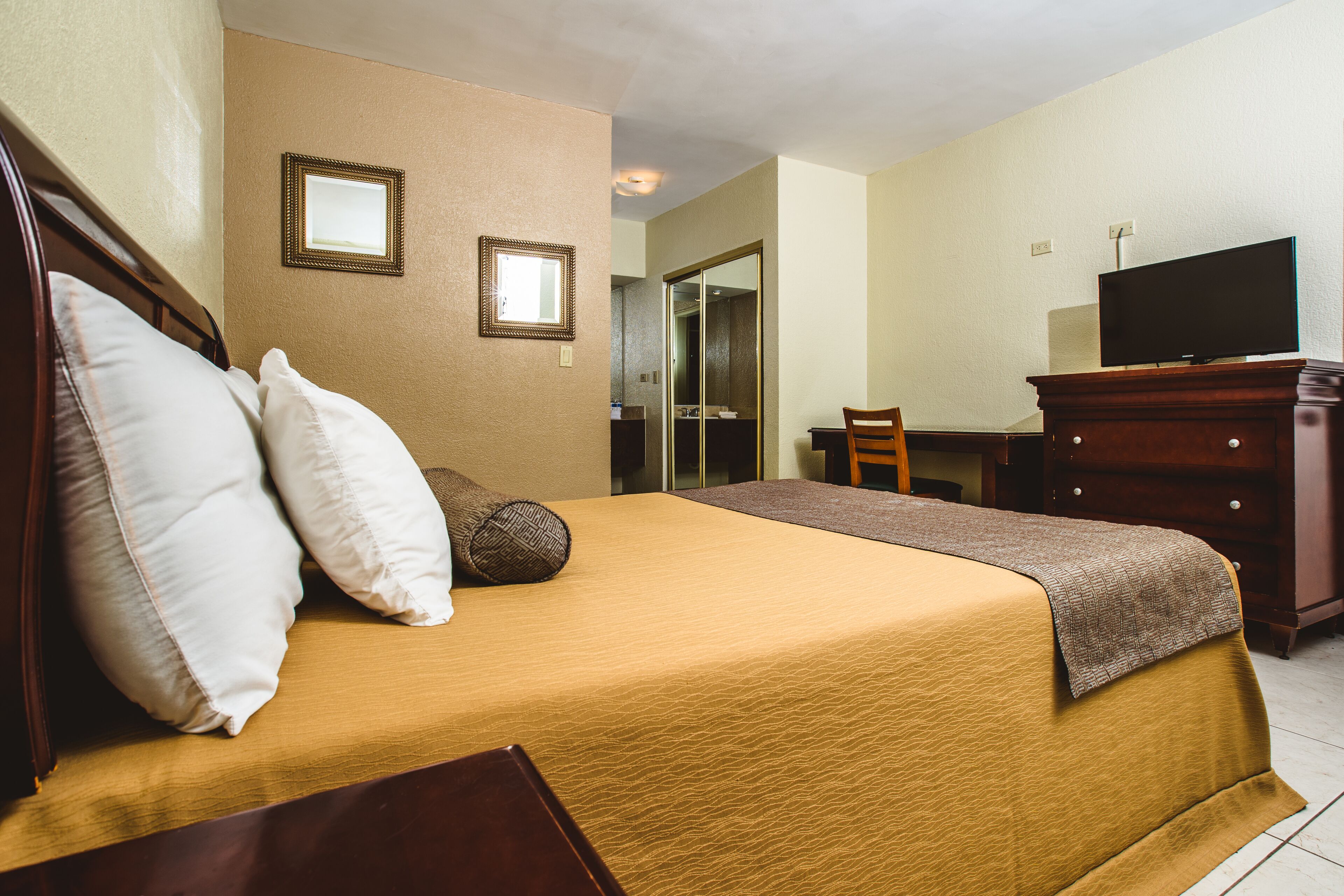 Habitació d'hotel amb llit, escriptori, televisió i mirall.