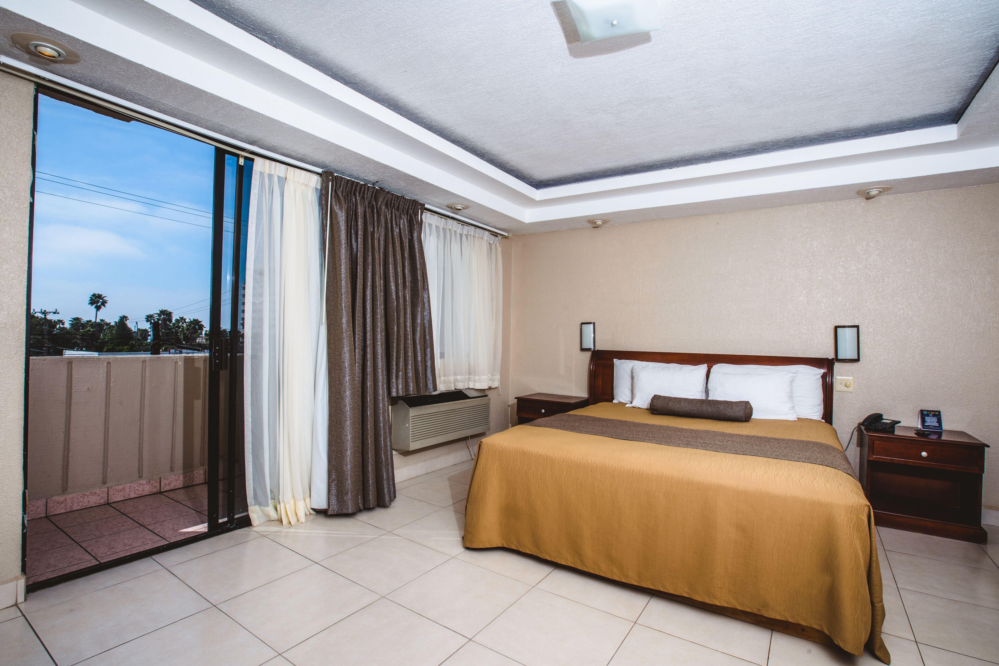 Una habitación de hotel con una cama grande, una mesita de noche, una ventana con cortinas y vistas al exterior.