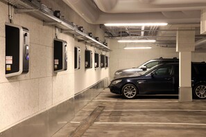 A parking garage with multiple parking spaces, a car in one of the spaces, and overhead fluorescent lighting.