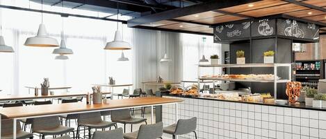 A modern kitchen with a central island, bar stools, pendant lighting, and a breakfast bar with various food items.