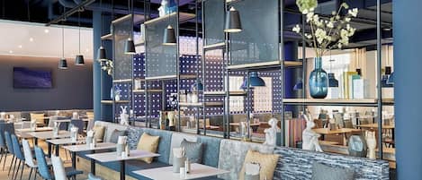 A modern restaurant with high tables and blue chairs, featuring a blue and white color scheme and decorative elements like vases and sculptures.