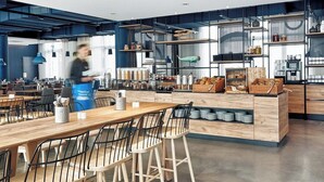 Una cocina moderna con una isla central, taburetes de bar y una persona al fondo.