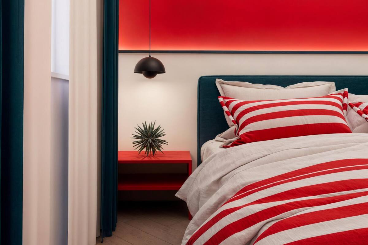 Ein modernes Schlafzimmer mit einer rot-weiß gestreiften Bettdecke, einem türkisfarbenen Kopfteil und einem kleinen Nachttisch mit einer Zierpflanze.