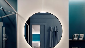Une salle de bain moderne avec un lavabo blanc, un miroir rond et un porte-serviettes.