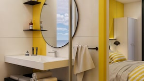 Une salle de bain moderne avec un meuble-lavabo blanc, un miroir rond et un mur d’accent jaune.
