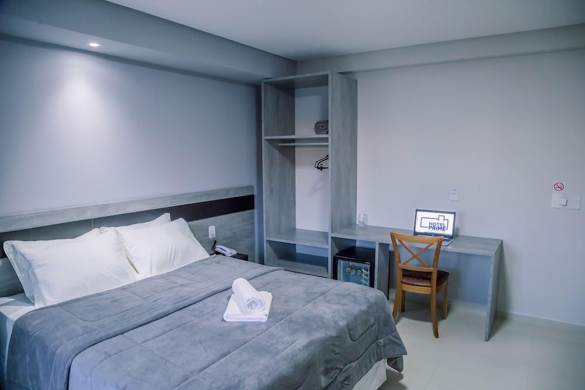 Una habitación de hotel con una cama, un escritorio, una silla y una pequeña estantería.