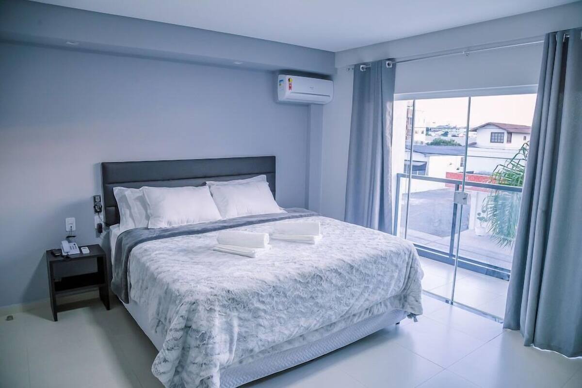 Un dormitorio con cama, mesita de noche, aire acondicionado y vistas a través de un ventanal grande.