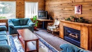 A cozy living room with a wooden interior, a fireplace, a television, and a sofa. - Bethlehem Centre (Nanaimo)