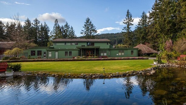 A large green house with a pond in front, surrounded by trees and a clear sky. - Bethlehem Centre (Nanaimo)