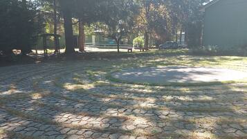 A paved courtyard with stone tiles, surrounded by trees and a building.