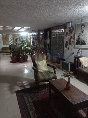 A spacious living room with a large armchair, several potted plants, a television, and a poster on the wall.