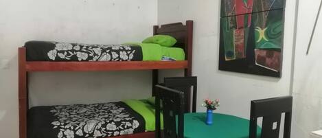 A dormitory room with two bunk beds, a small table with a green tablecloth, and a chair.