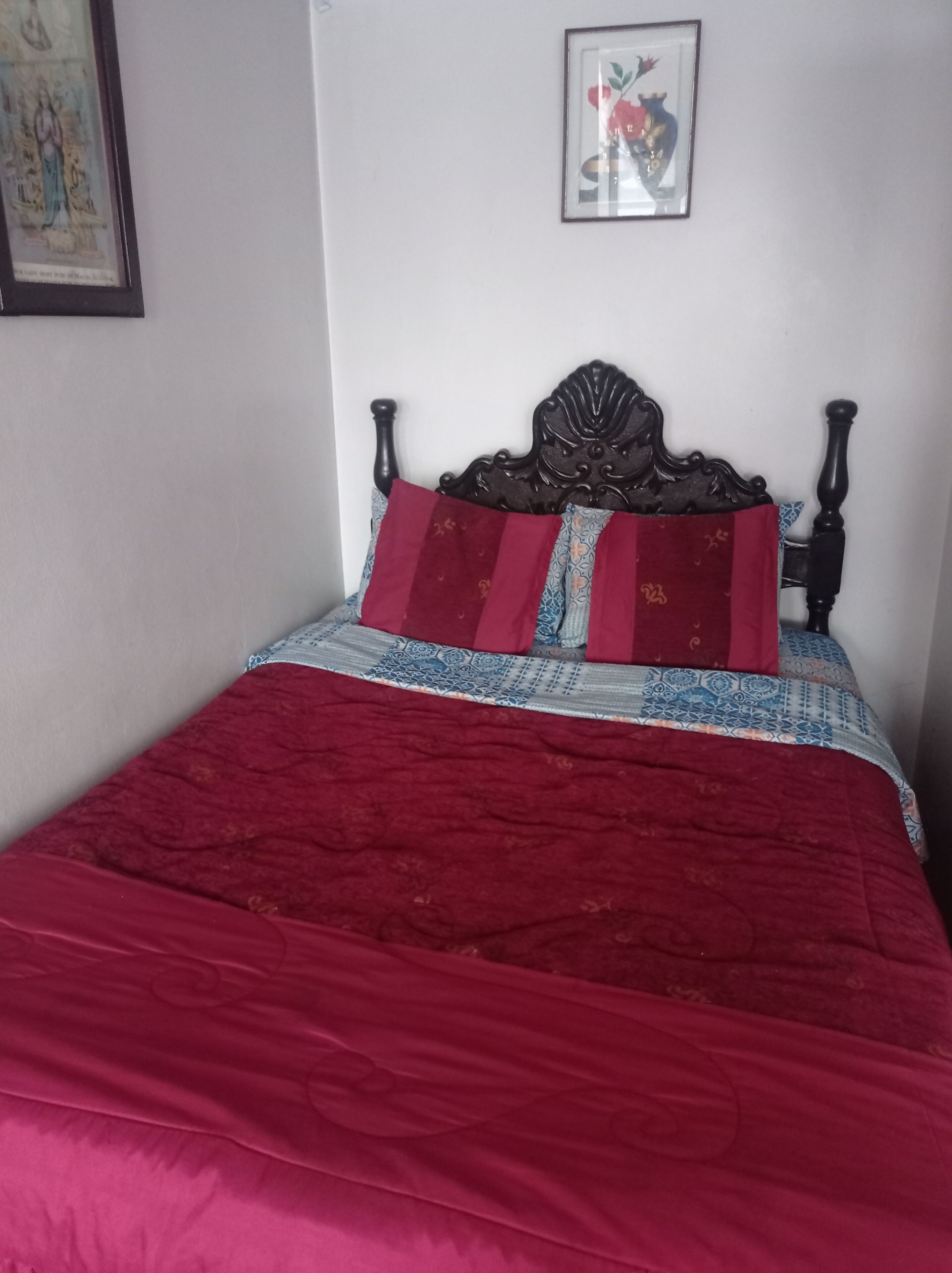 A bed with a dark wooden headboard, a red and patterned bedspread, and two red pillows.