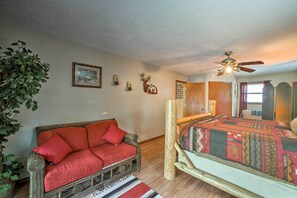 A room with a wooden bed, a wicker sofa, a ceiling fan, and a large plant. - Waterfront Home w/ Fire Pit on Table Rock Lake (Golden)