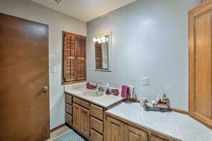 A bathroom with a wooden door, a white sink, a mirror with lights, and a wooden vanity. - Waterfront Home w/ Fire Pit on Table Rock Lake (Golden)