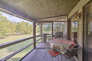 A covered outdoor area with a table and chairs, a grill, and a view of a grassy yard and trees. - Waterfront Home w/ Fire Pit on Table Rock Lake (Golden)