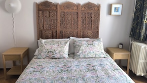 Una camera da letto con una coperta a fiori, un poggiatesta in legno, comodini e un termosifone.