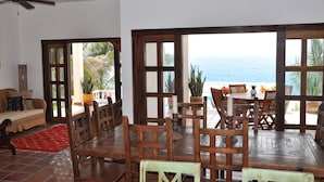 Una habitación con una mesa de comedor y sillas de madera, un sofá y vistas al océano a través de amplios ventanales.