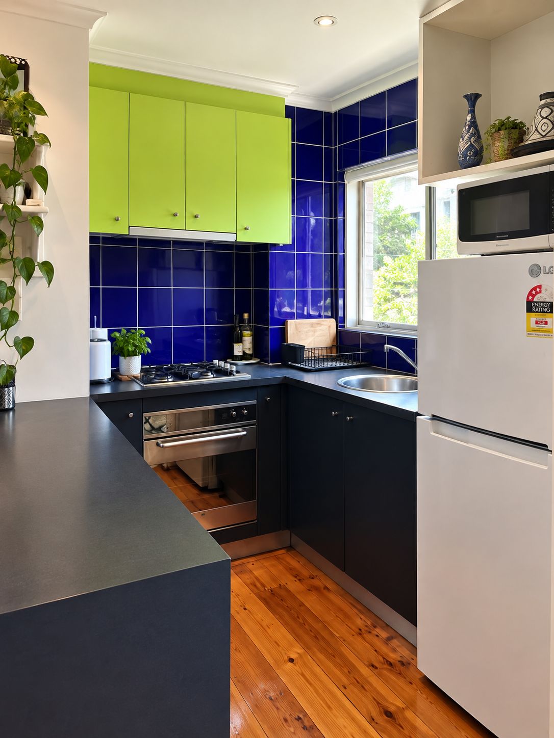 A modern kitchen with green cabinets, a microwave, and a sink.