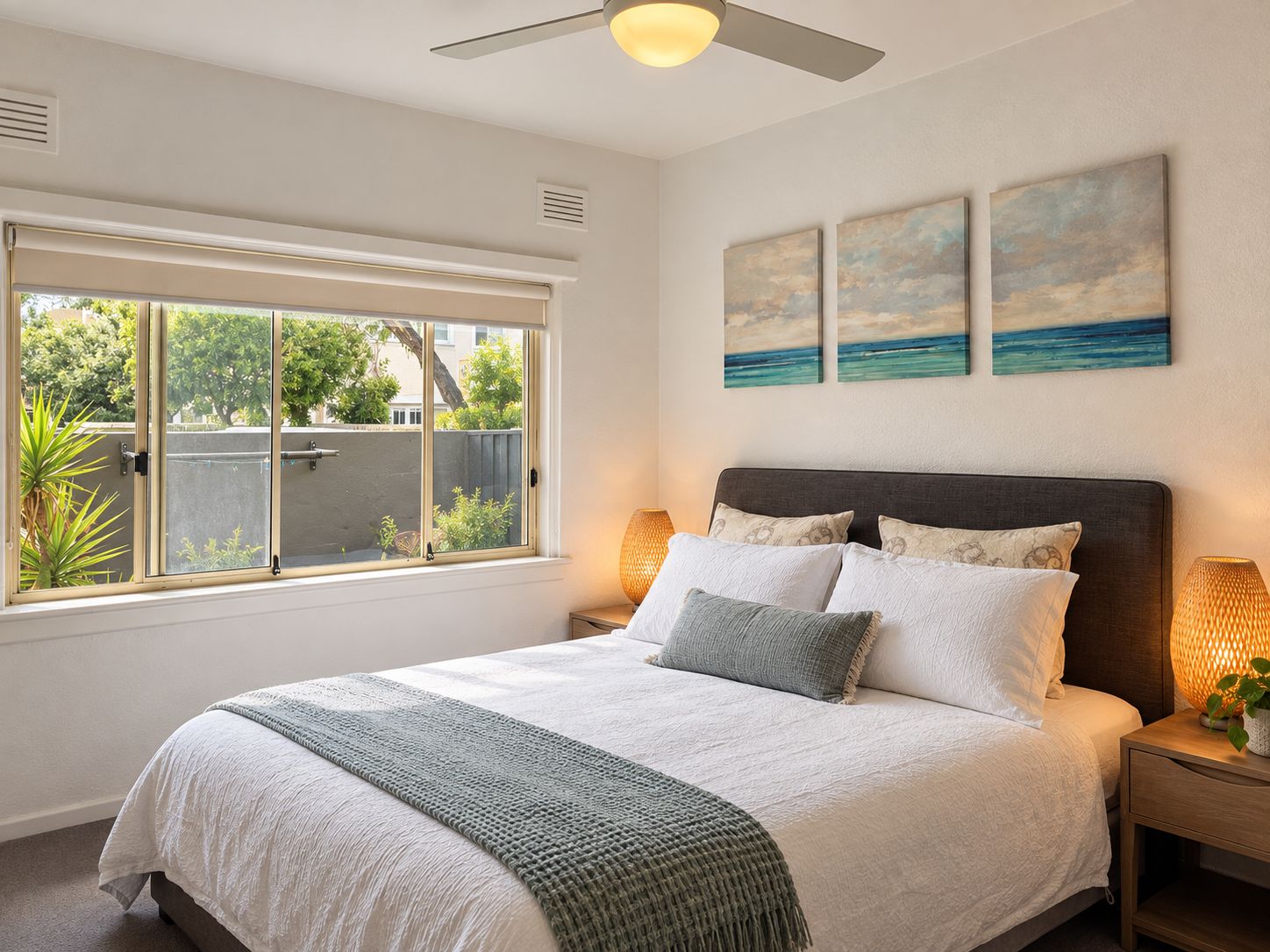 Une chambre à coucher avec un lit, une fenêtre, un ventilateur de plafond et des œuvres d’art murales.