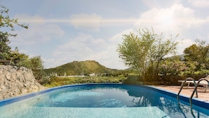 A clear swimming pool with a stone wall on one side and a view of a hill in the background. - Monte Argentario, Tuscany, whole villa with panoramic view. (Monte Argentario)