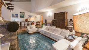 A spacious living area with a large sofa, a coffee table, and a fireplace. There is a staircase with wooden beams and a view of the outdoors. - Monte Argentario, Tuscany, whole villa with panoramic view. (Monte Argentario)