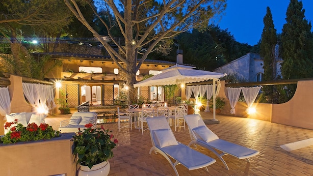 An outdoor patio with lounge chairs, a dining area, and a large tree providing shade. - Monte Argentario, Tuscany, whole villa with panoramic view. (Monte Argentario)