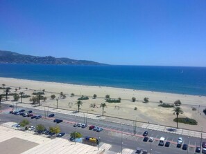 A beach view with a parking lot and a road in the foreground.