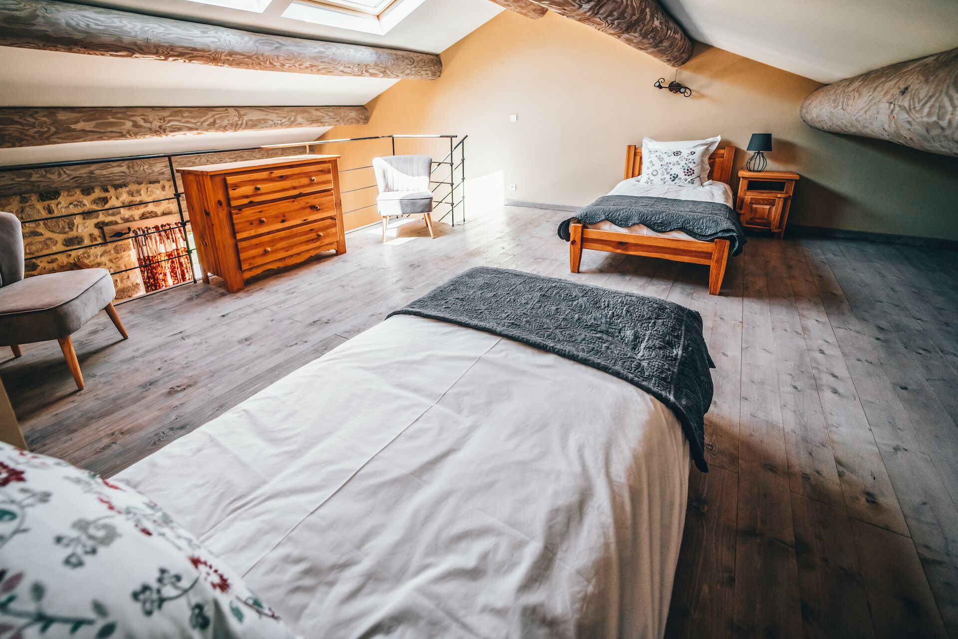 A cozy attic bedroom with a large bed, a smaller bed, a wooden dresser, and a chair.
