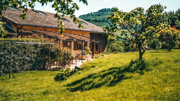 A stone building with a tiled roof, surrounded by lush greenery and a hilly landscape. - gite / house ardéchoise of character with swimming pool (Labatie-D'andaure)