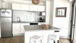 A modern kitchen with white cabinetry, a stainless steel refrigerator, a built-in microwave, and a coffee maker. There is a small island with two white barstools and a decorative plant. - Breathtaking sea view  (Quiberon)