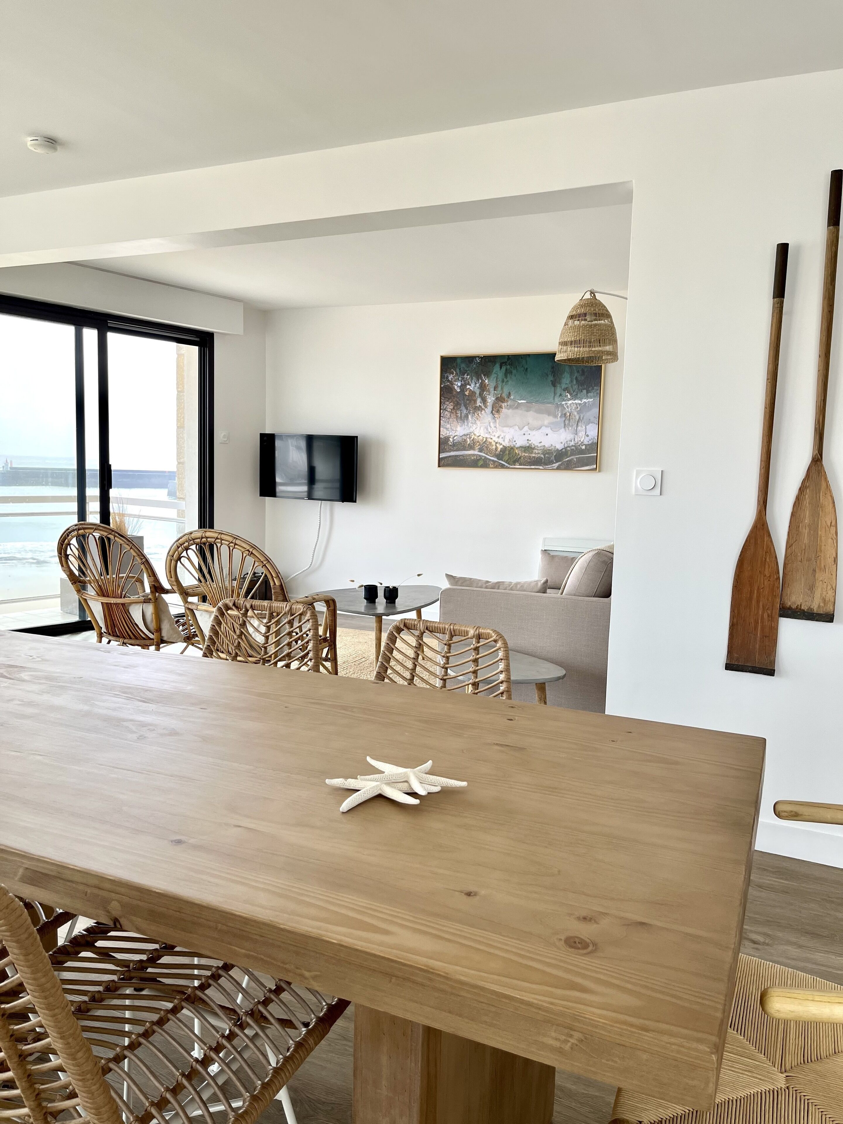 Un salon moderne avec une table à manger en bois, des chaises en osier, un canapé et un tableau accroché au mur.