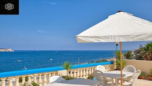 An outdoor terrace with a table and chairs, overlooking a coastal view with the sea and boats.