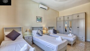 A hotel room with two beds, a wardrobe, a nightstand with a lamp, and an air conditioning unit.