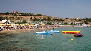 A beach with boats, umbrellas, and a crowd of people.