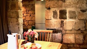 Un muro de piedra rústico, una mesa de madera con una jarra y un cuenco de fruta, y una silla.