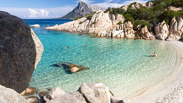 A coastal beach with clear turquoise water, rocky formations, and a mountainous backdrop. - Holiday apartments L'Ea di Lavru 
Studio apartment TOP INTERIOR DESIGN (Porto San Paolo)