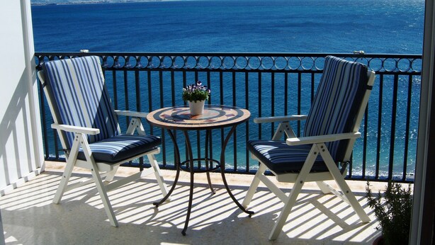 A balcony with two striped chairs, a small round table with a potted plant, and a view of the sea. - Enchanting apartment, 1st beach line, panoramic views, parking, fast internet (Almuñécar)
