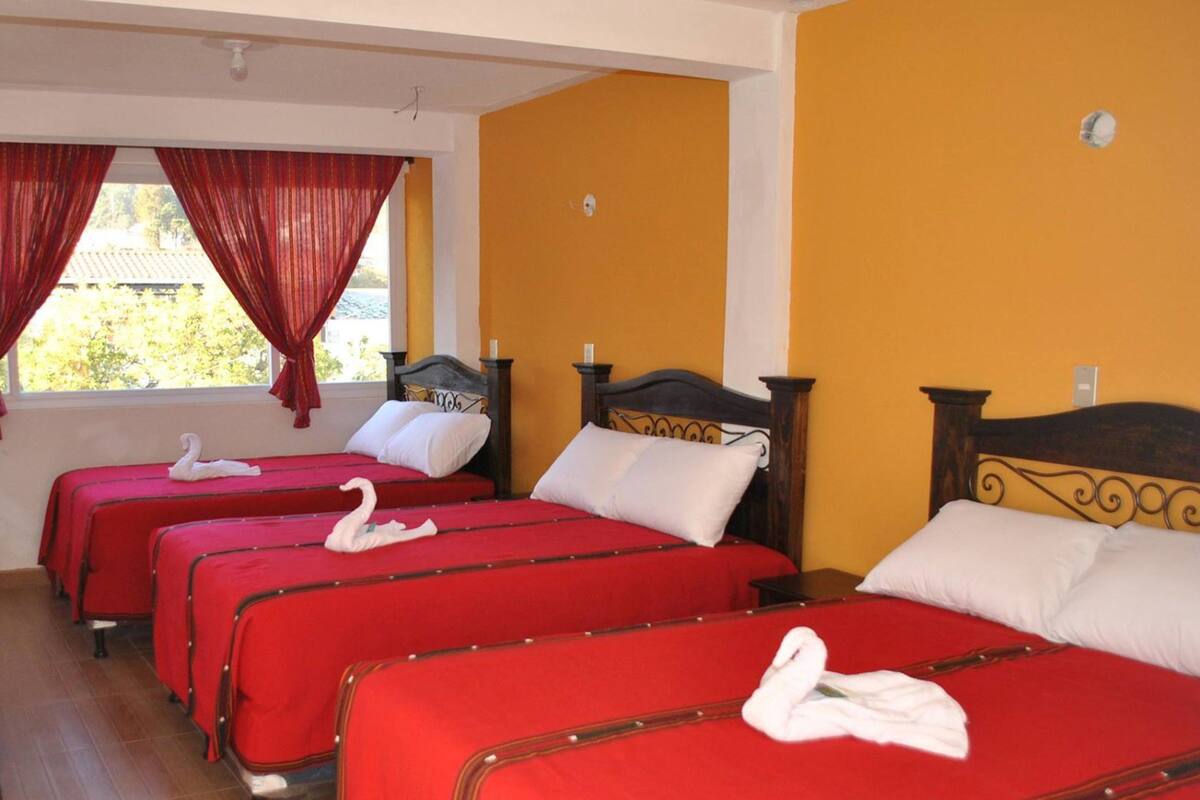 Une chambre d’hôtel avec quatre lits simples, chacun recouvert d’une courtepointe rouge et agrémenté de deux oreillers blancs, et un cygne décoratif posé sur chaque lit.