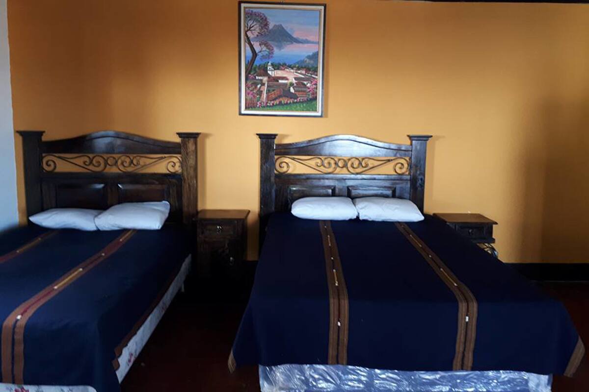 Une chambre avec deux lits, chacun doté d’une tête de lit en bois et d’une couvre-lit bleue. Un tableau est accroché au mur, au-dessus des lits.